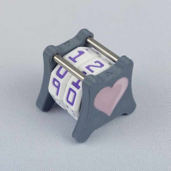 The NC-2 number counter viewed from an isometric angle showing the top dials and side 2 heart. The version shown has a dark gray base and a pink heart in the middle on both sides 1 and 2.